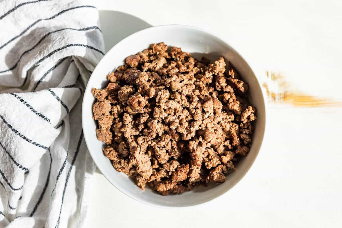 Browned ground beef in a white bowl with a striped linen on the side.