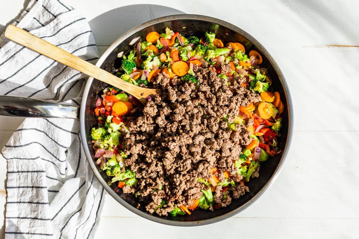 Adding the ground beef to the finished veggies along with the stir fry sauce in the large skillet.