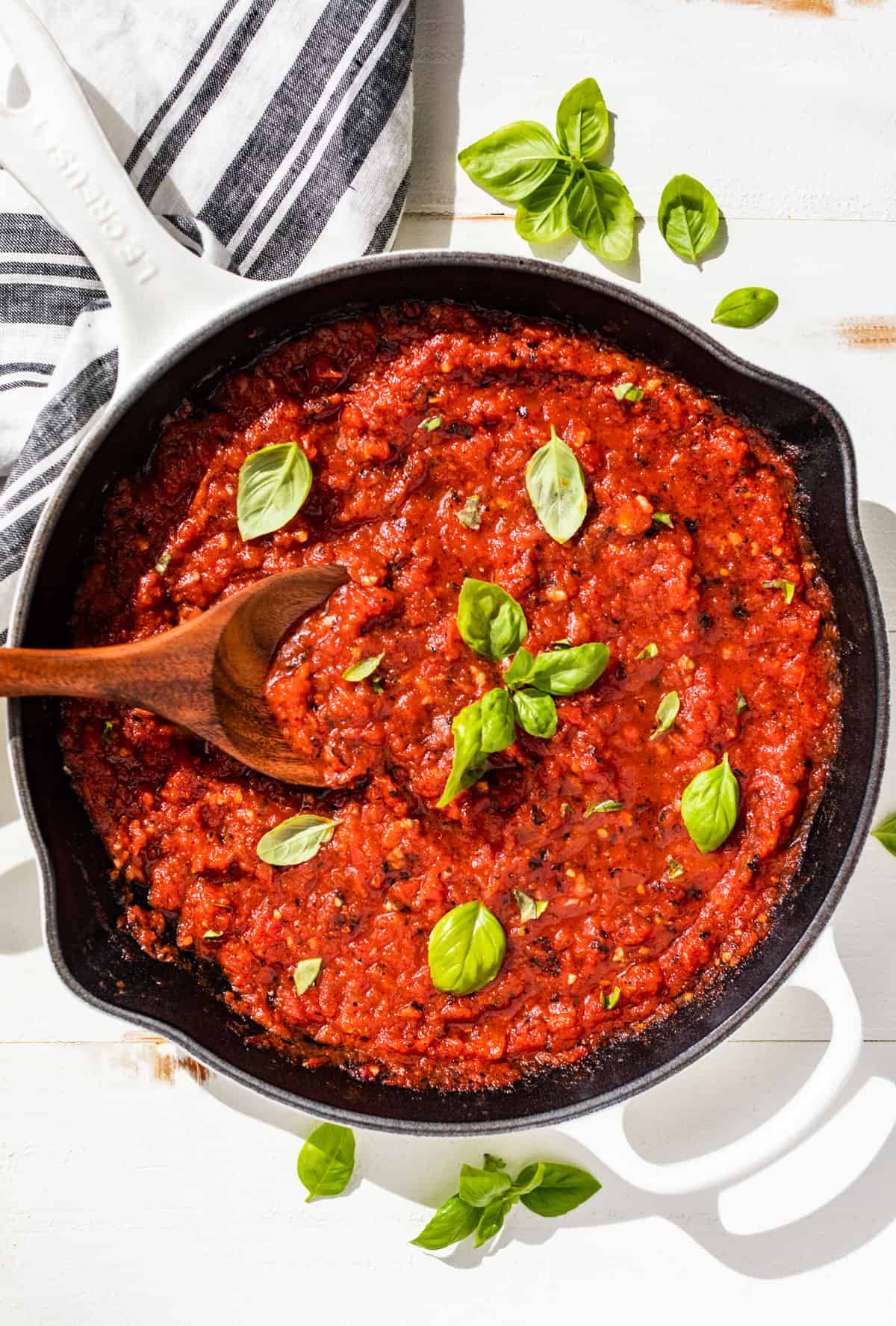 Straight down view of Marinara Sauce in a white skillet with basil leaves on top.