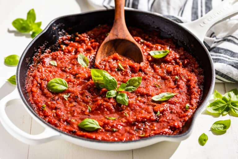 Finished Marinara Sauce in a white skillet topped with sprigs of basil.
