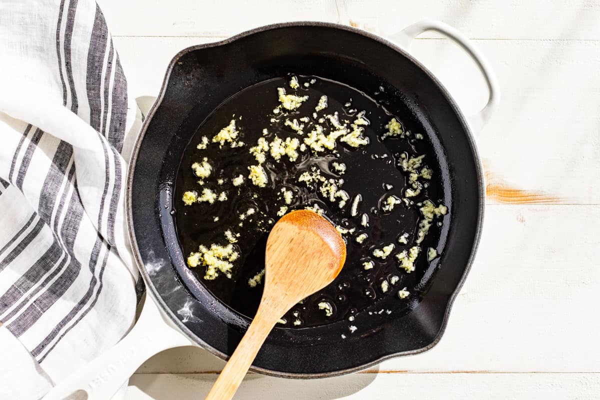 Sautéing garlic in olive oil in a white skillet.