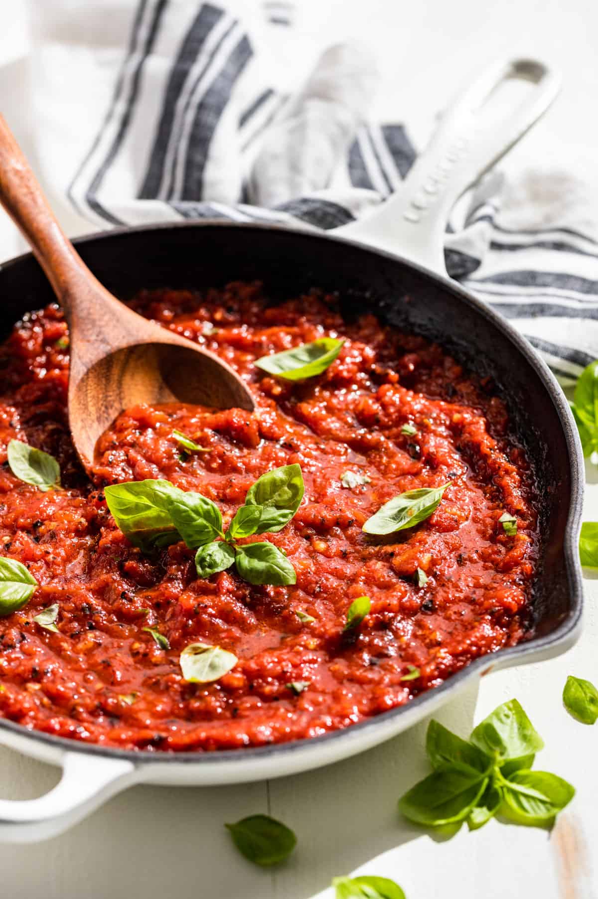Side view of Marinara Sauce in a white skillet topped with sprigs of basil.