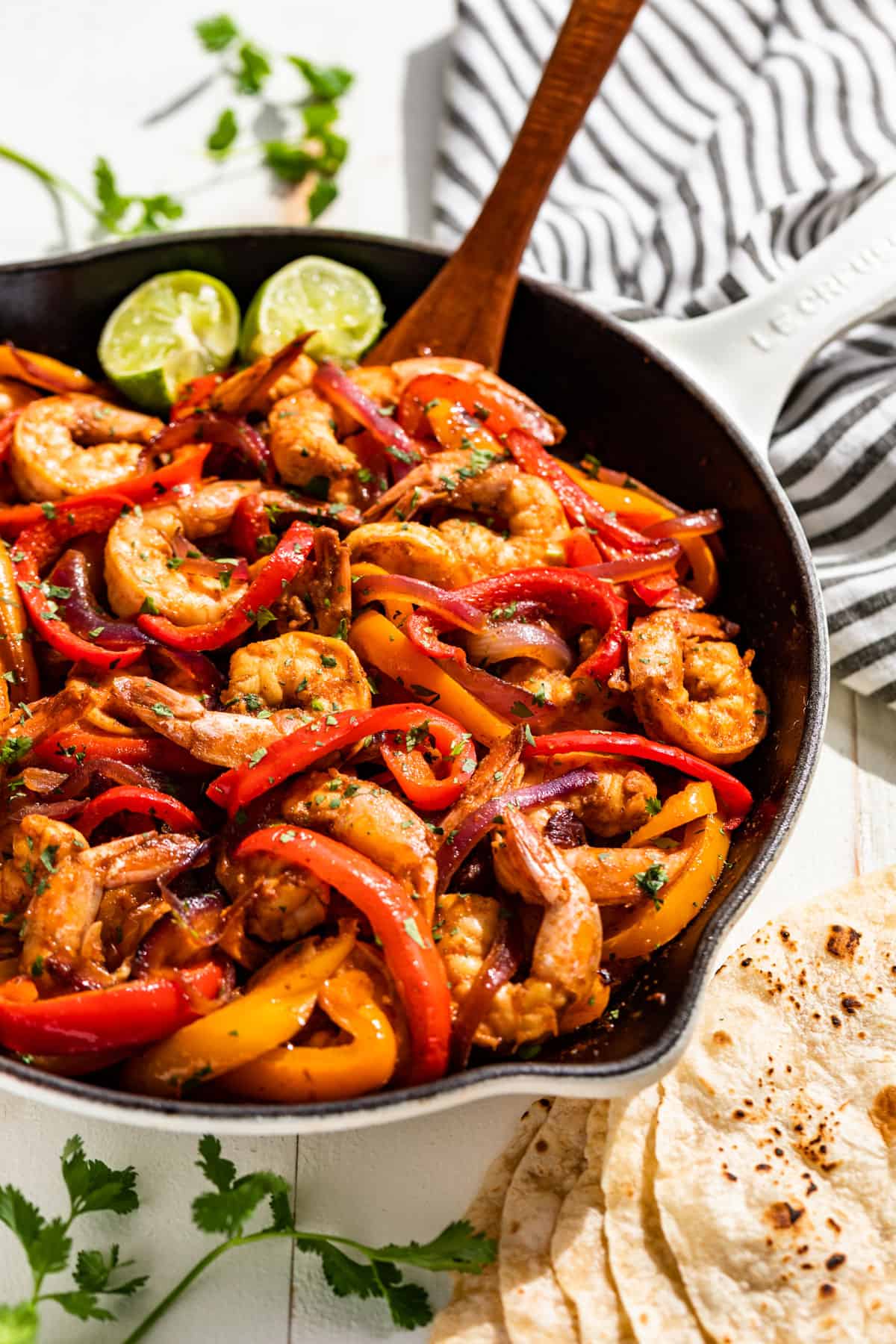 Side view of a white skillet filled with Shrimp Fajitas topped with lime wedges.