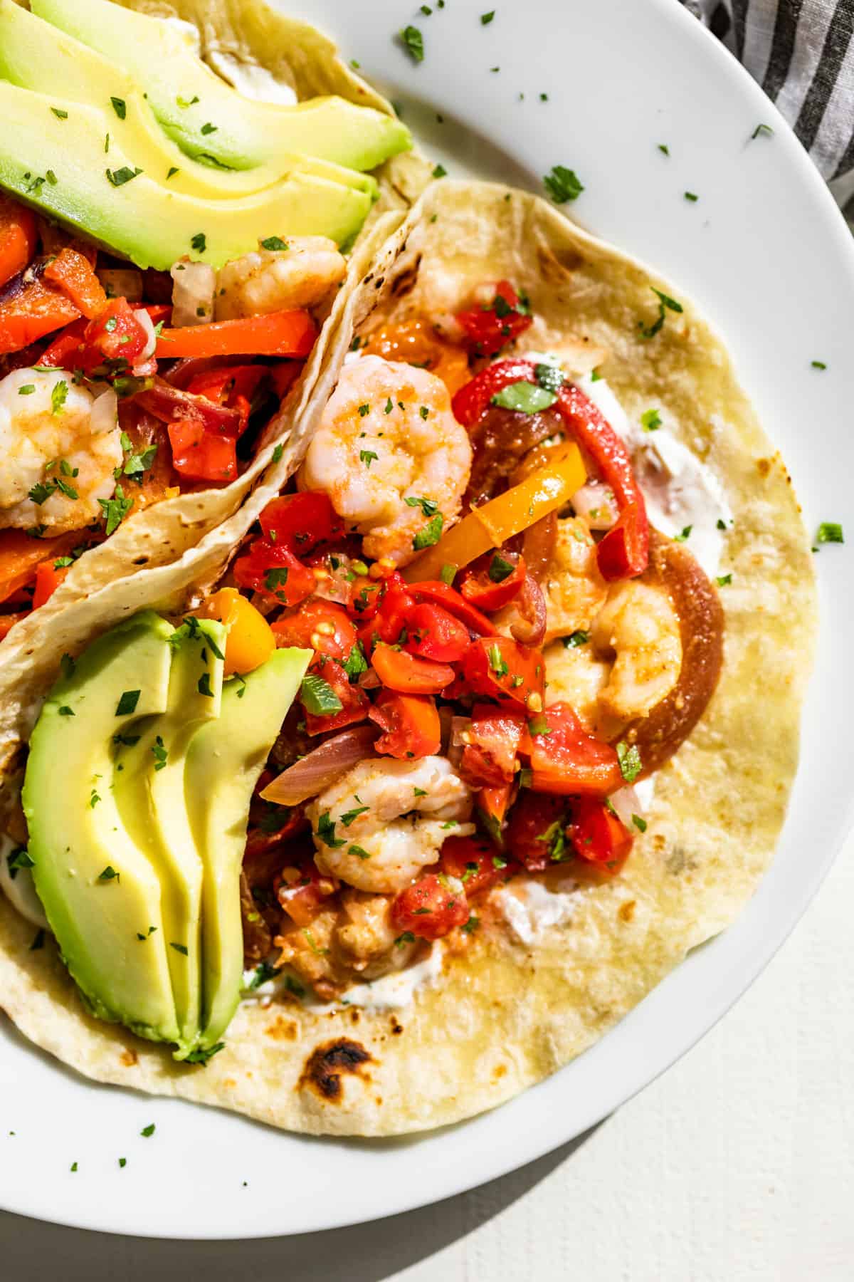 Shrimp Fajita on a tortilla shell with avocado slices, sour cream, and chopped cilantro.