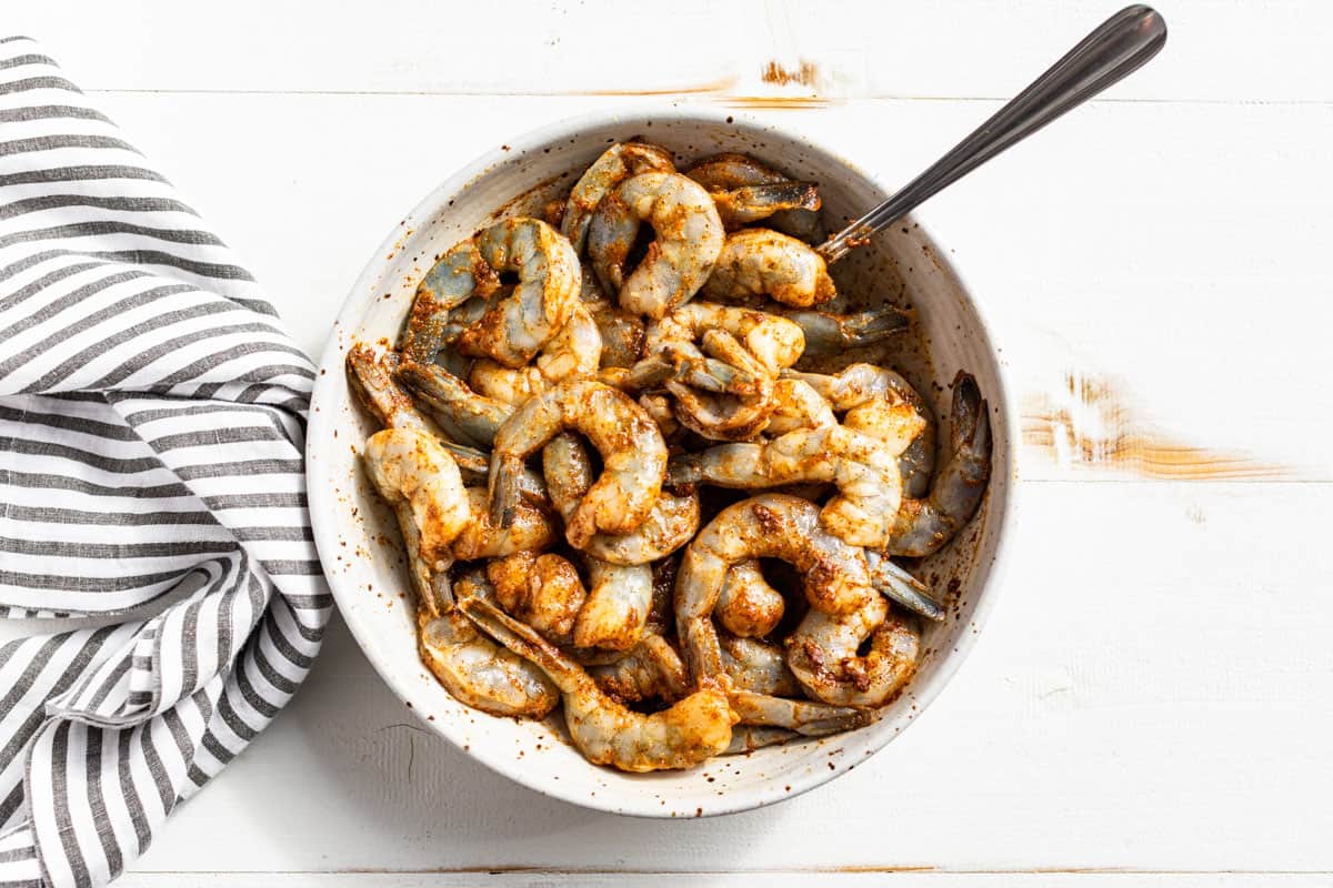 Shrimp being mixed with Fajita Seasoning in a white bowl.