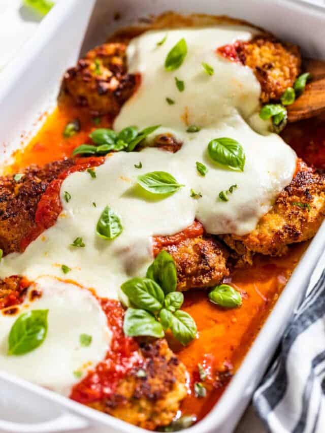 Side view of Chicken Parmesan in a white baking dish topped with basil sprigs.