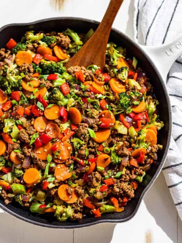 A large white skillet filled with Ground Beef Stir Fry with a wooden spatula scooping some out.