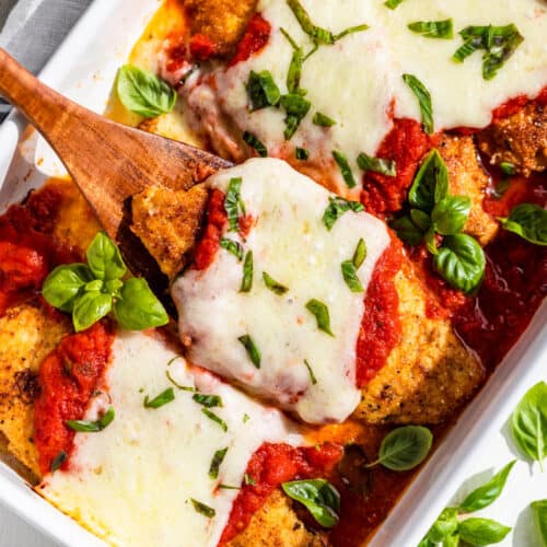 Straight down view of finished Almond Flour Chicken Parmesan topped with basil and a wooden spatula lifting 1 chicken cutlet out.