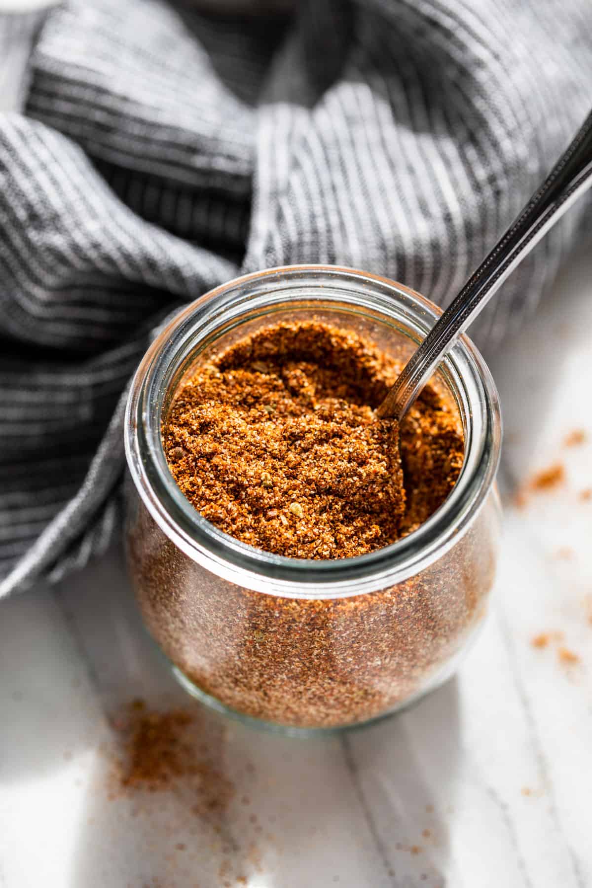 Looking down on a glass jar of Fajita Seasoning with a silver spoon in it.