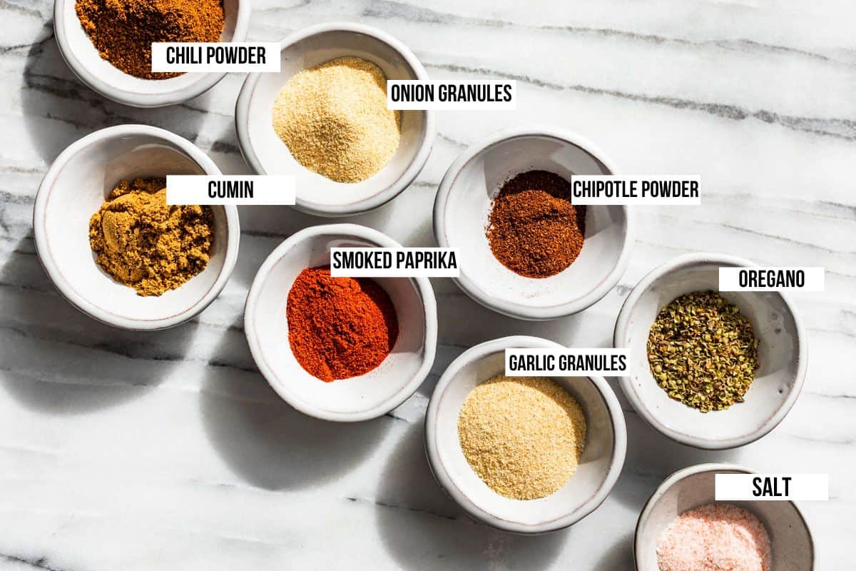 All the spices for Fajita Seasoning in small bowls, chili powder, cumin, smoked paprika, onion powder, garlic powder, oregano, and chipotle powder.