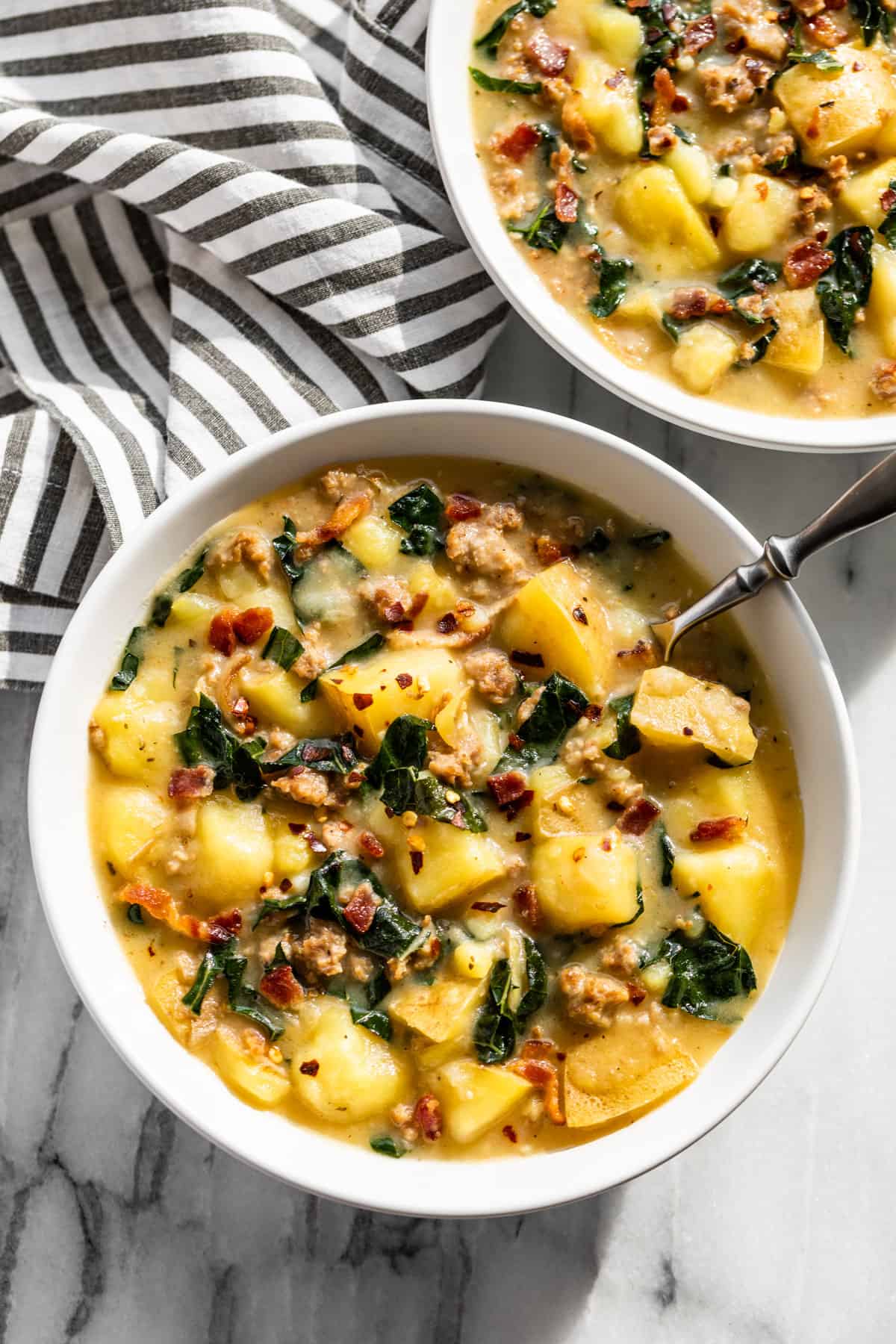Two bowls of Zuppa Toscana with a silver spoon in one.