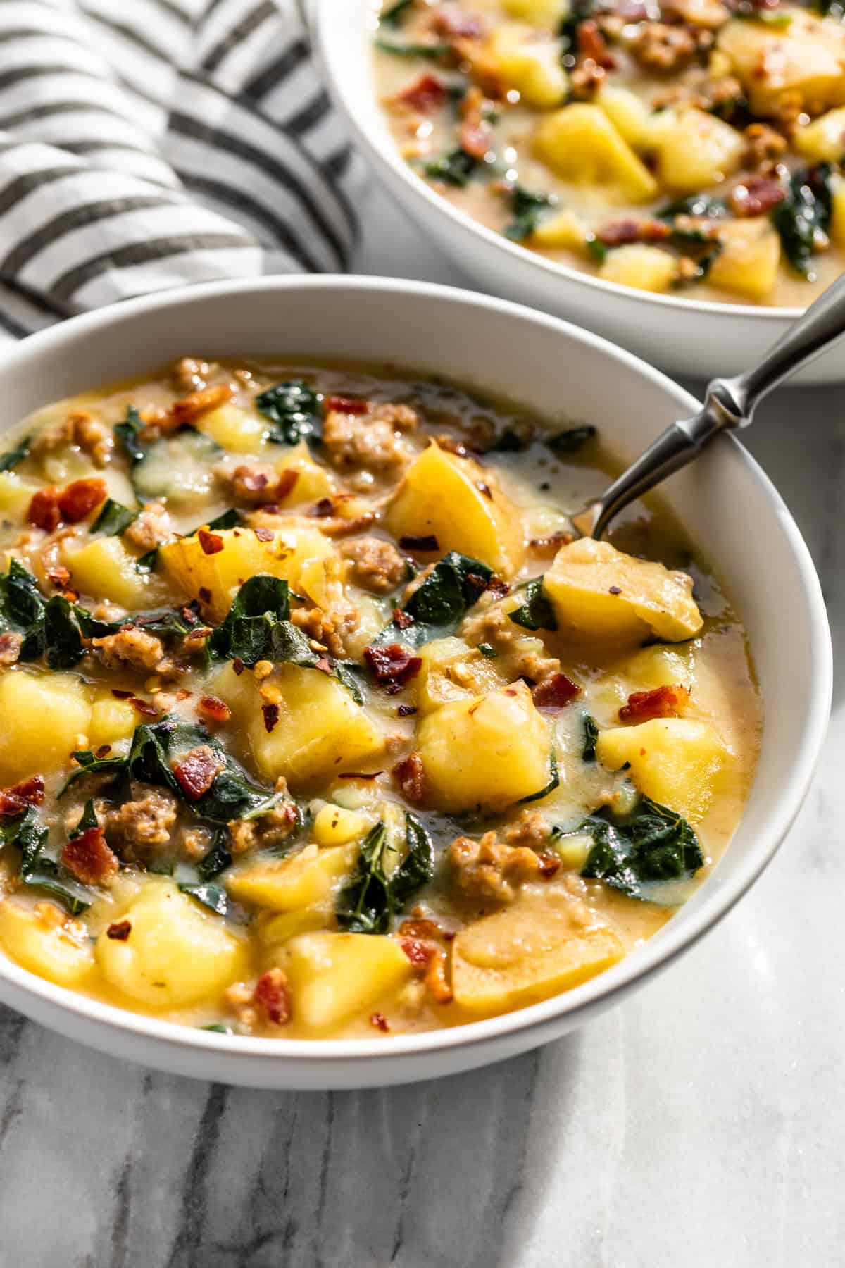 Side view of Zuppa Toscana in white serving bowls with a striped linen on the side.