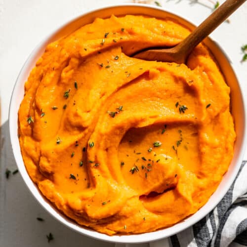Finished Mashed Sweet Potatoes in a white bowl with a blue and white striped linen on the side.