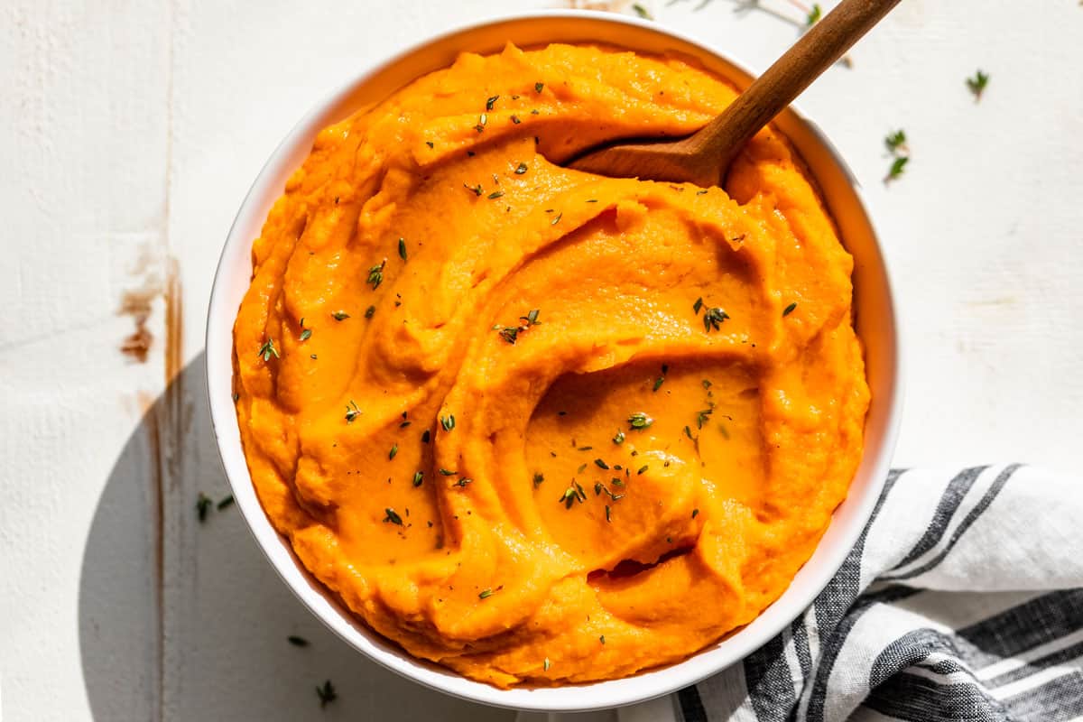 Finished Mashed Sweet Potatoes in a white bowl with a blue and white striped linen on the side.