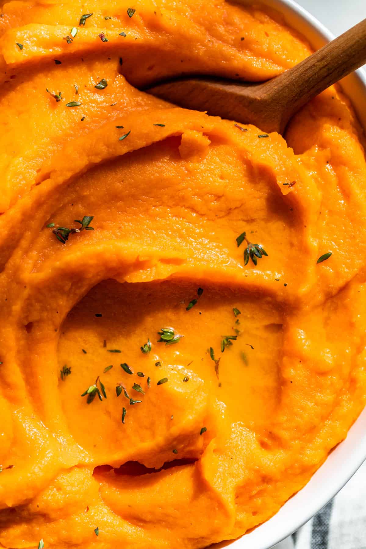 Close view of Mashed Sweet Potatoes in a white bowl with a wood spoon.