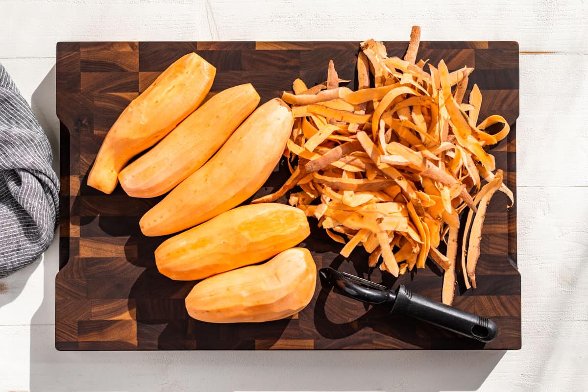 Peeling the sweet potatoes on a wood cutting board.