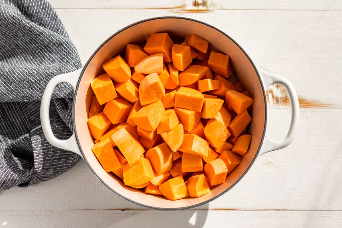 Adding the cubed sweet potatoes to the butter and cream mixture in a large white pot.
