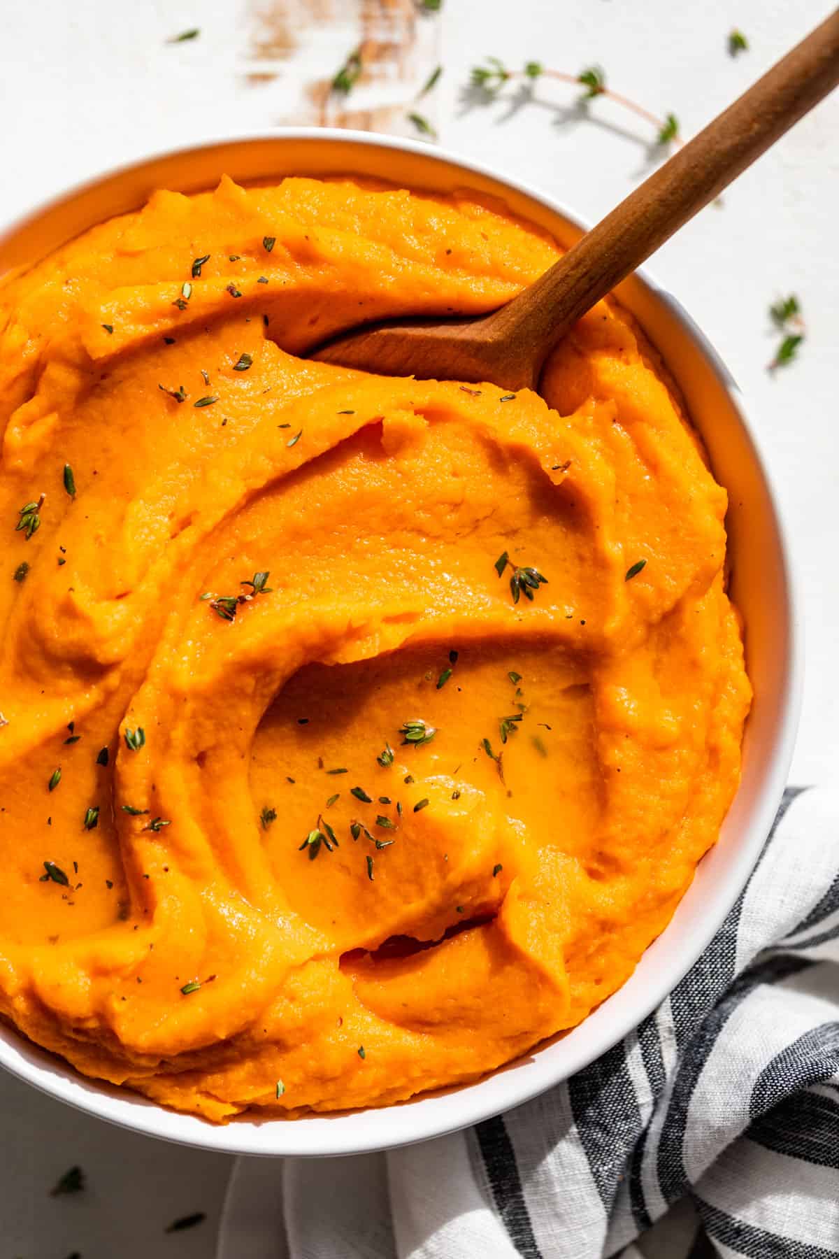 Downwards view of Mashed Sweet Potatoes in a white bowl with a wooden spoon.