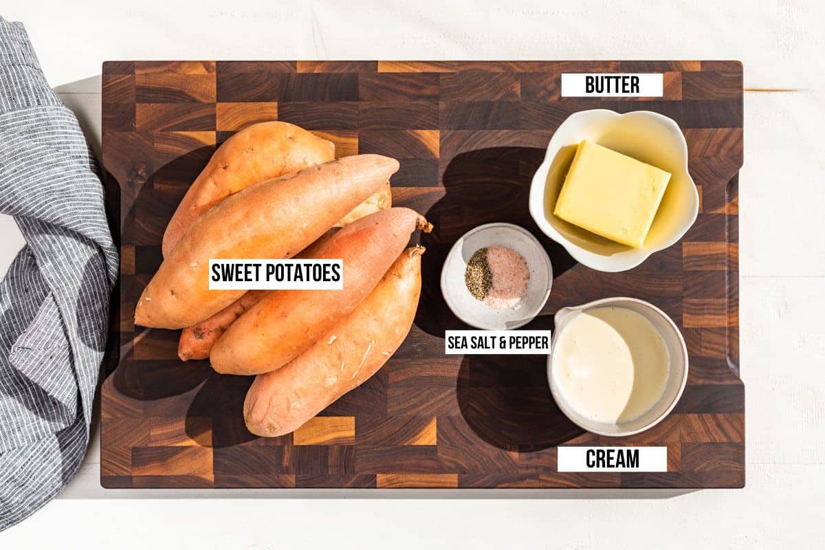 Sweet potatoes, butter, cream, sea salt, and pepper on a wood cutting board.
