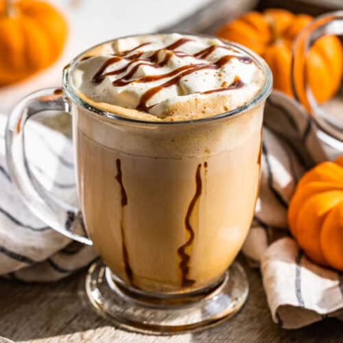 Two mugs of Pumpkin Chai Latte topped with whipped cream and caramel sauce with mini pumpkins around the glass mugs.