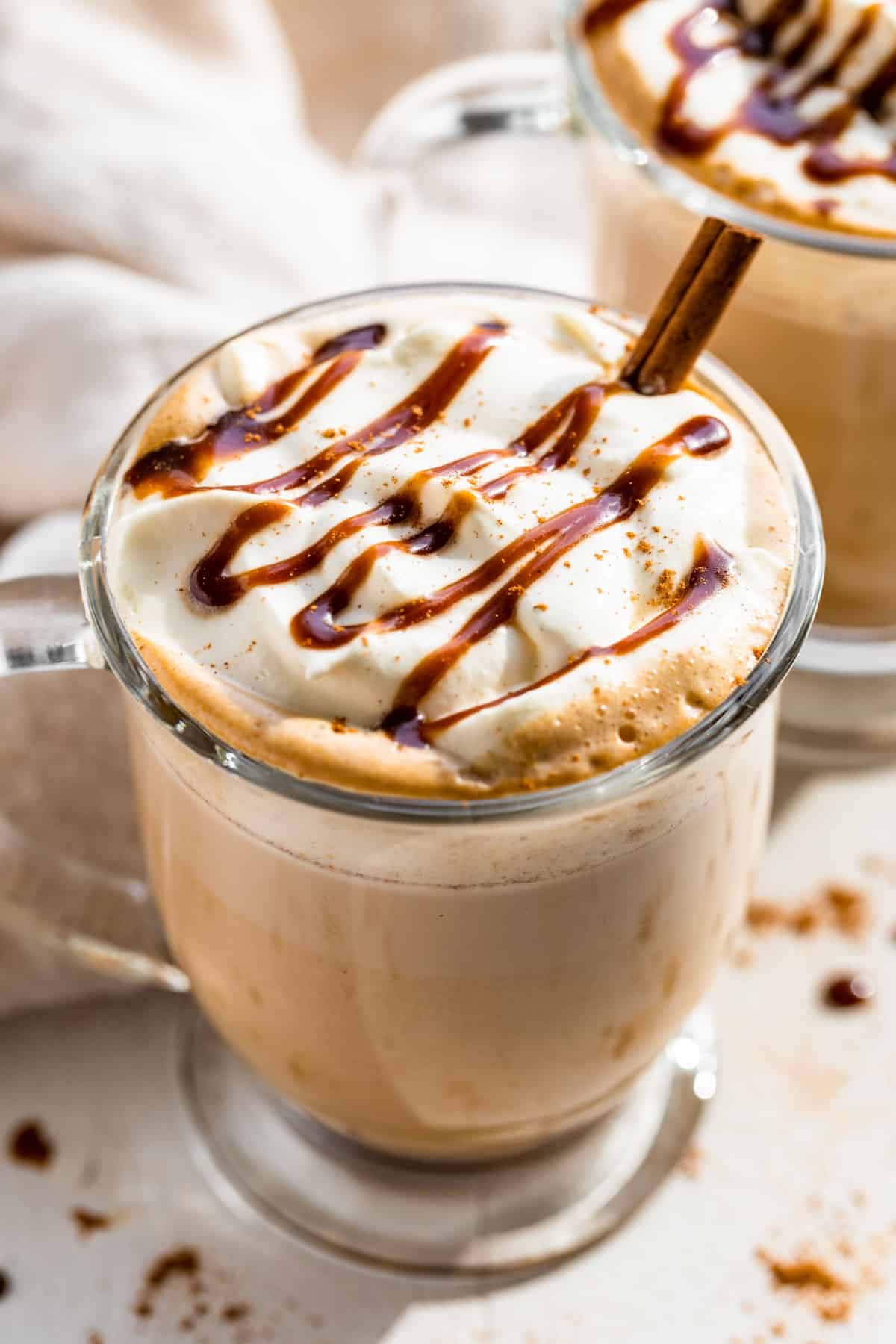 Two glass mugs filled with Pumpkin Chai Latte topped with whipped cream and drizzled with caramel sauce.