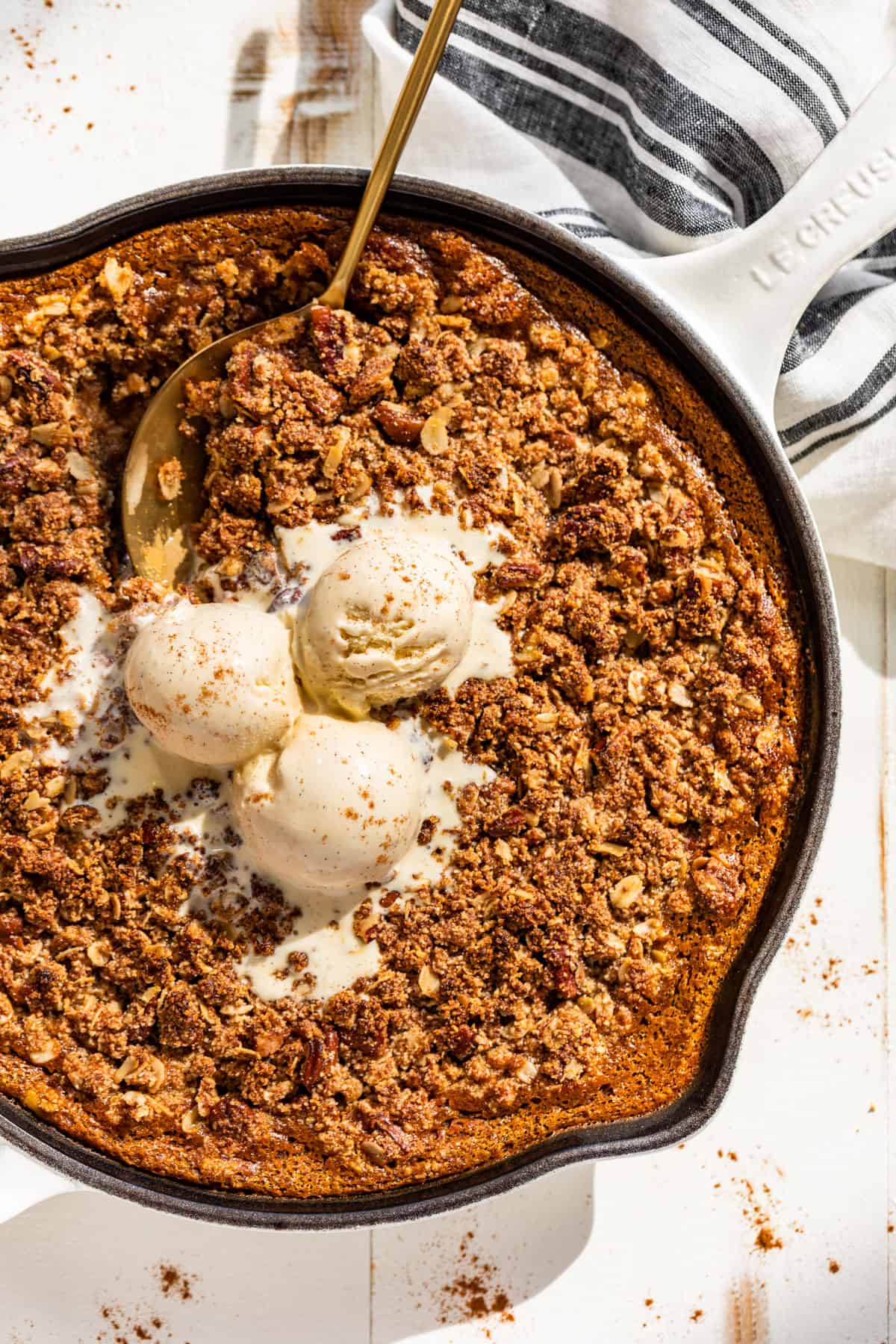 Downwards view of Pumpkin Crisp in a white skillet topped with scoops of ice cream.