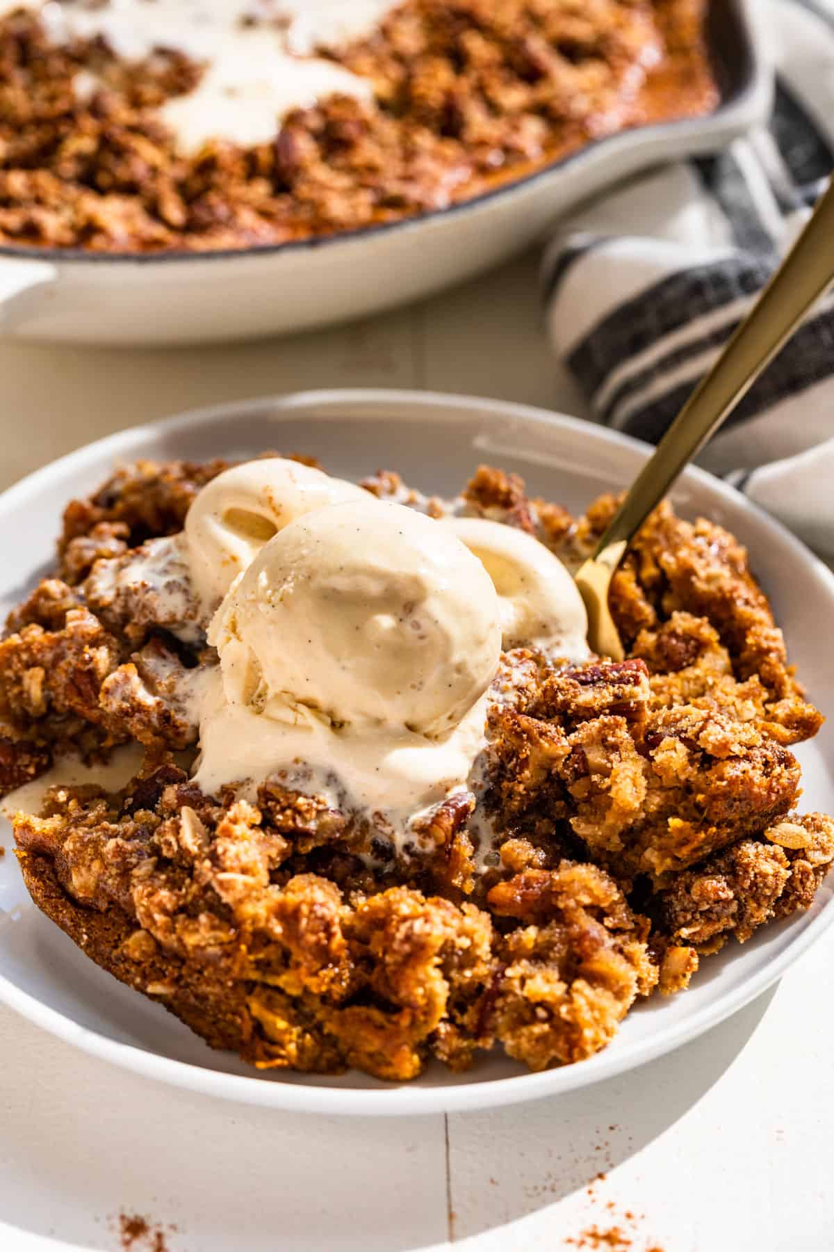 Close view of Pumpkin Crisp on a white plate topped with a scoop of vanilla ice cream.
