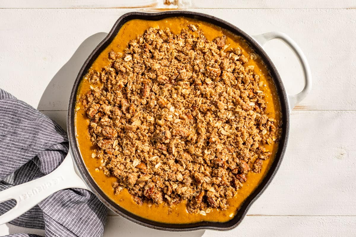 The pumpkin pie filling being topped with crisp topping.