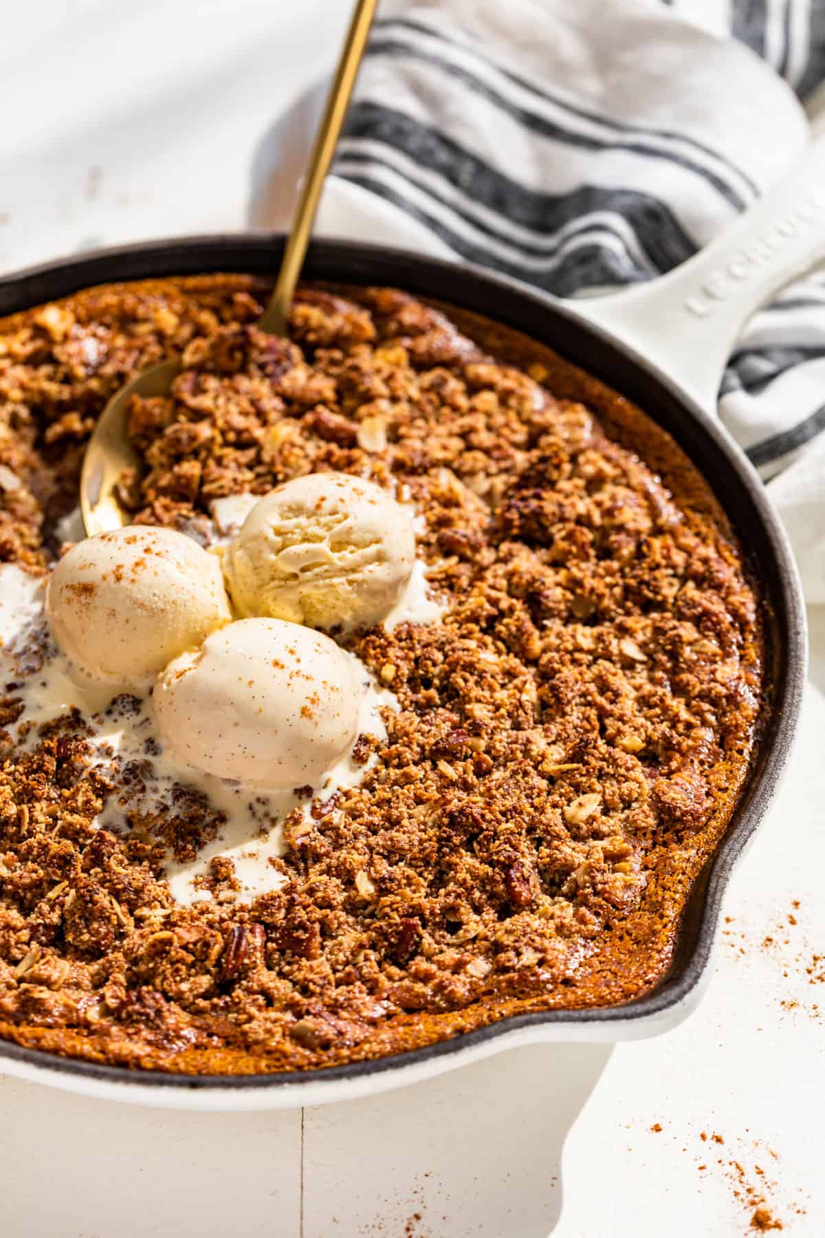 Side view of Pumpkin Crisp in a white skillet topped with vanilla ice cream.