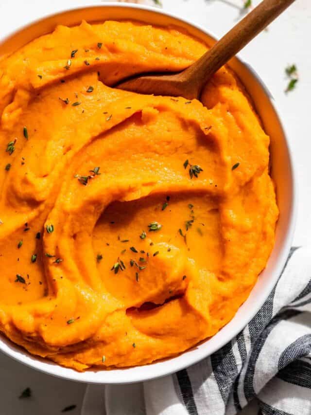 Downwards view of Mashed Sweet Potatoes in a white bowl with a wooden spoon.