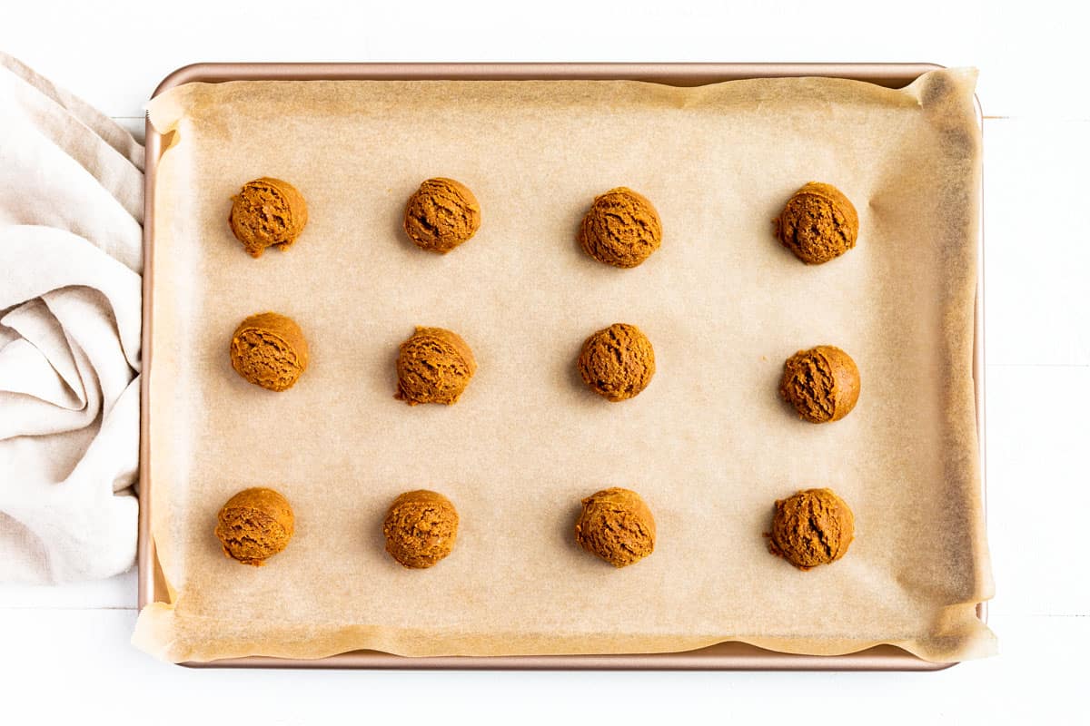 Portioned out peanut butter cookie dough rolled into smooth balls on a parchment lined baking sheet.