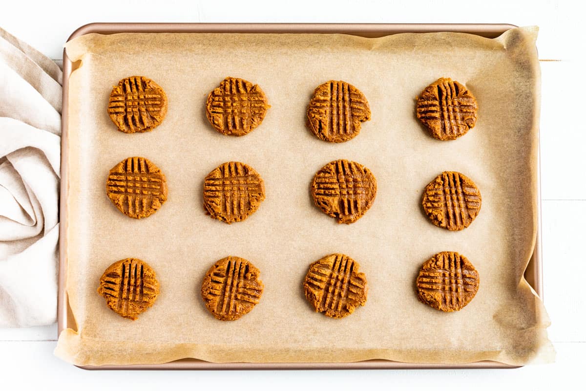 Flattening the peanut butter cookie dough balls with a criss cross pattern with a fork.