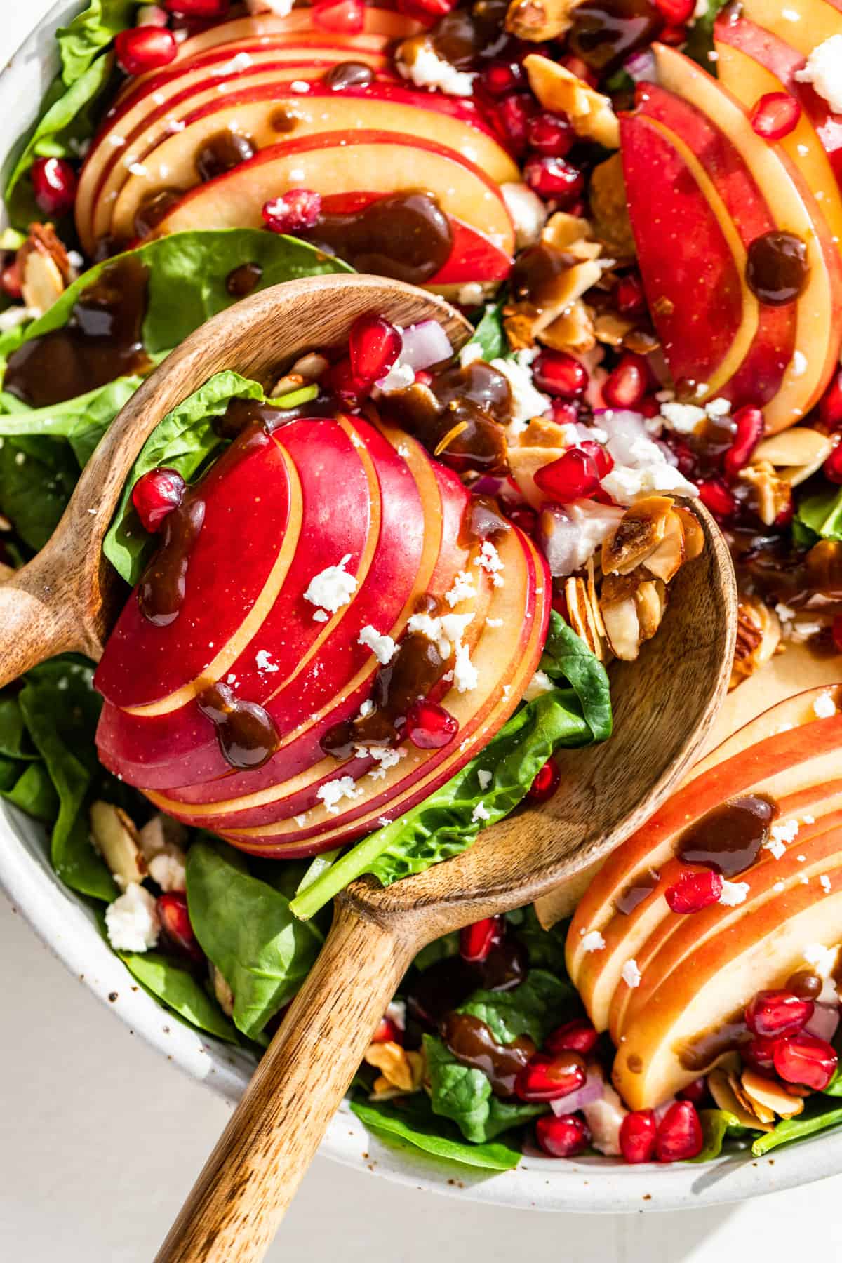 Close up view of Apple Spinach Salad with wooden spoons scooping some out.