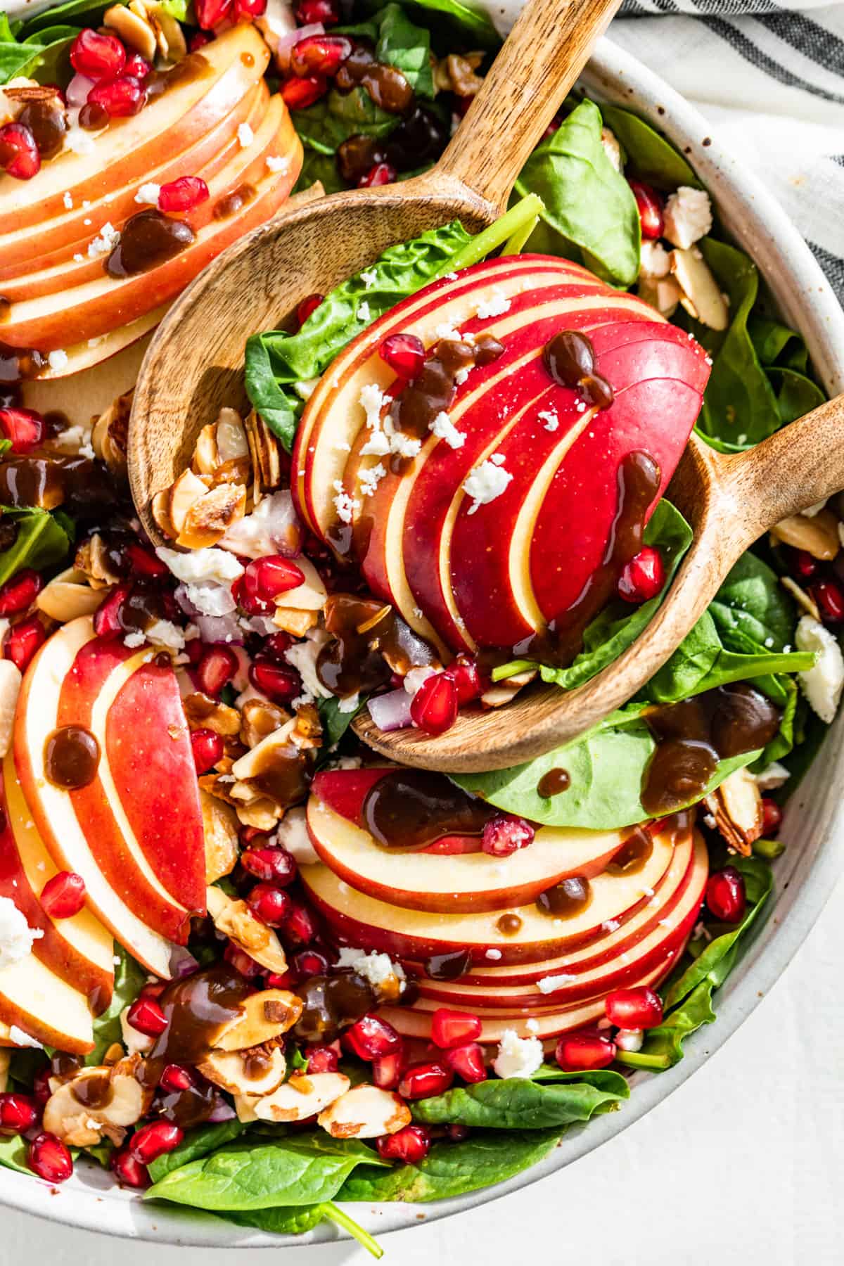 Straight down view of Apple Spinach Salad drizzled with balsamic vinaigrette with wooden serving spoons scooping some out.