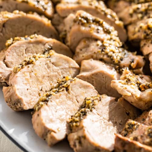 Close up side view of a few slices baked pork tenderloin on a serving platter.
