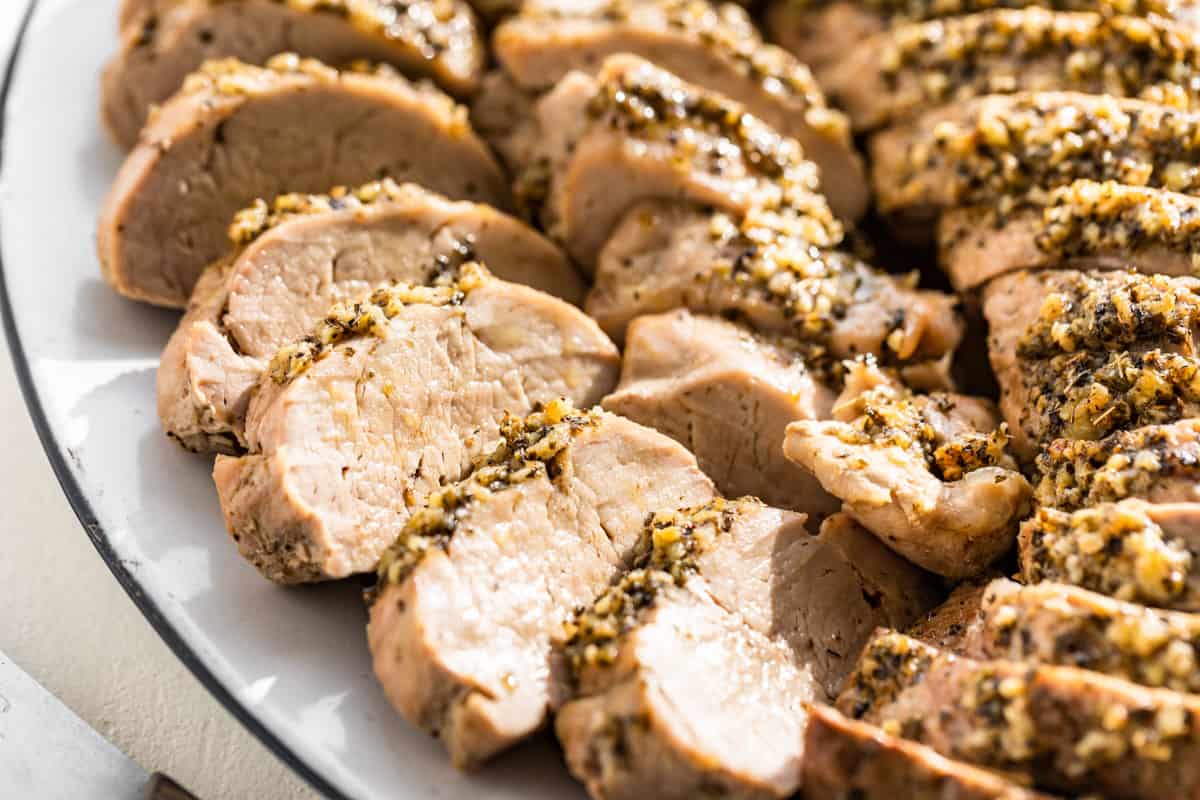 Close up side view of a few slices baked pork tenderloin on a serving platter.