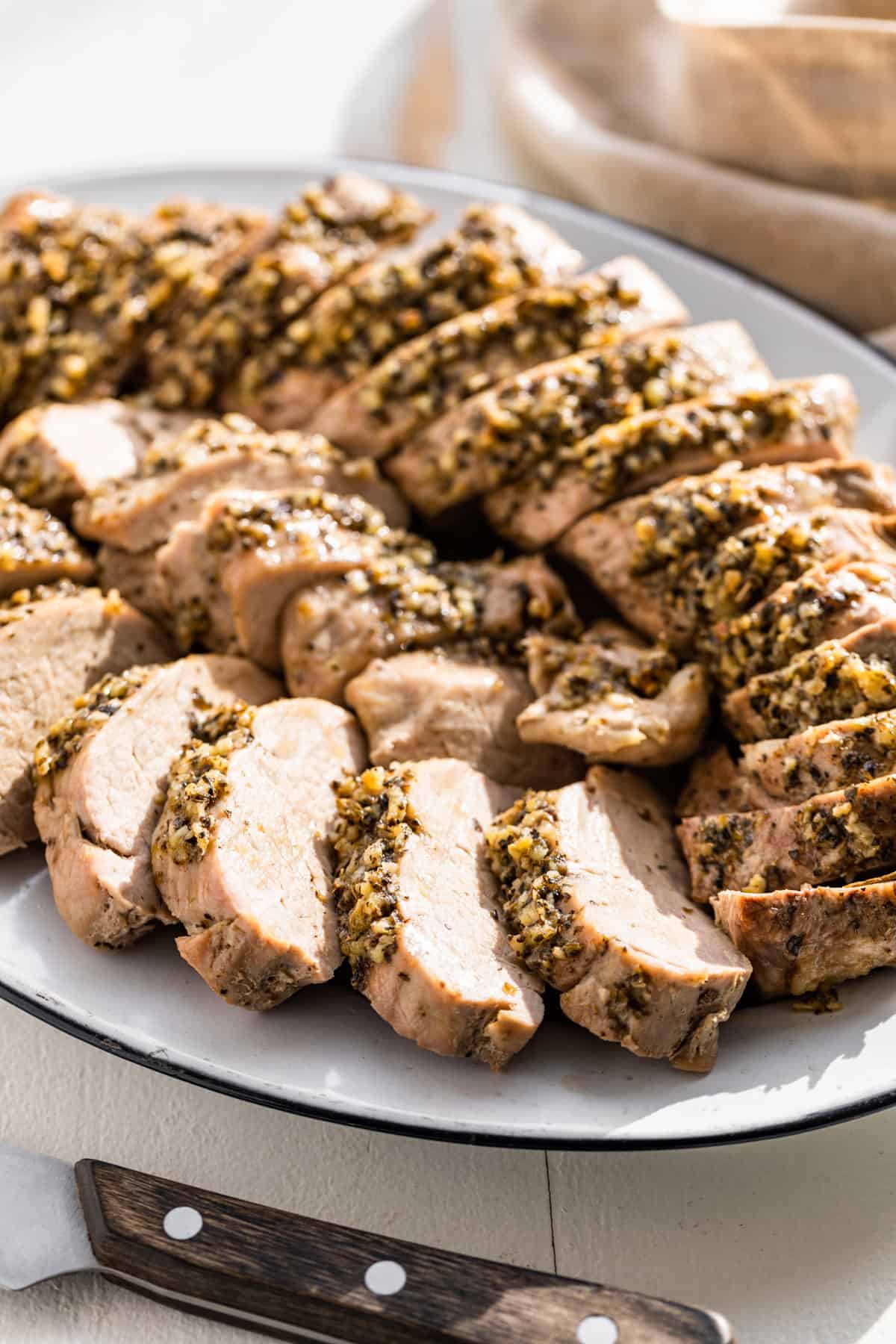 Side view of sliced Pork Tenderloin laid in a circle on a platter with a wood handled knife in the front.