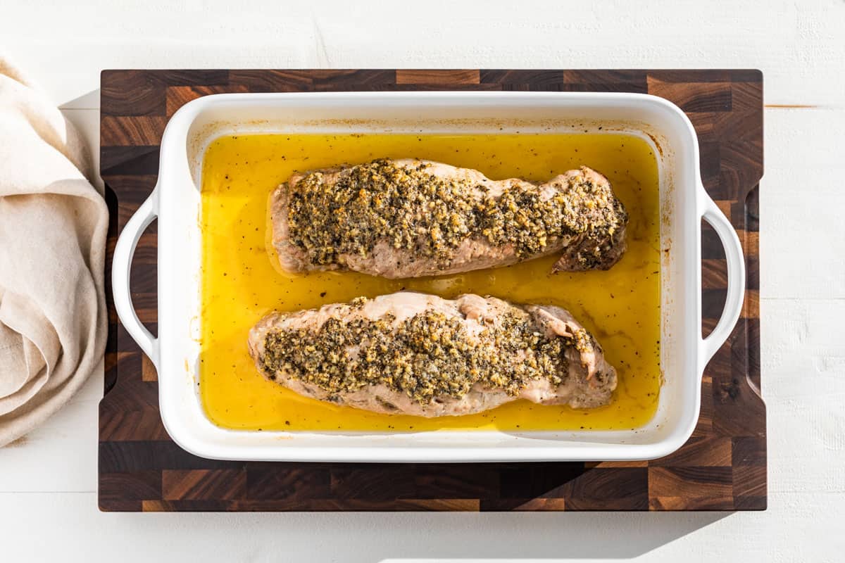 Baked Pork Tenderloin surrounded by it's juices in a white baking dish.