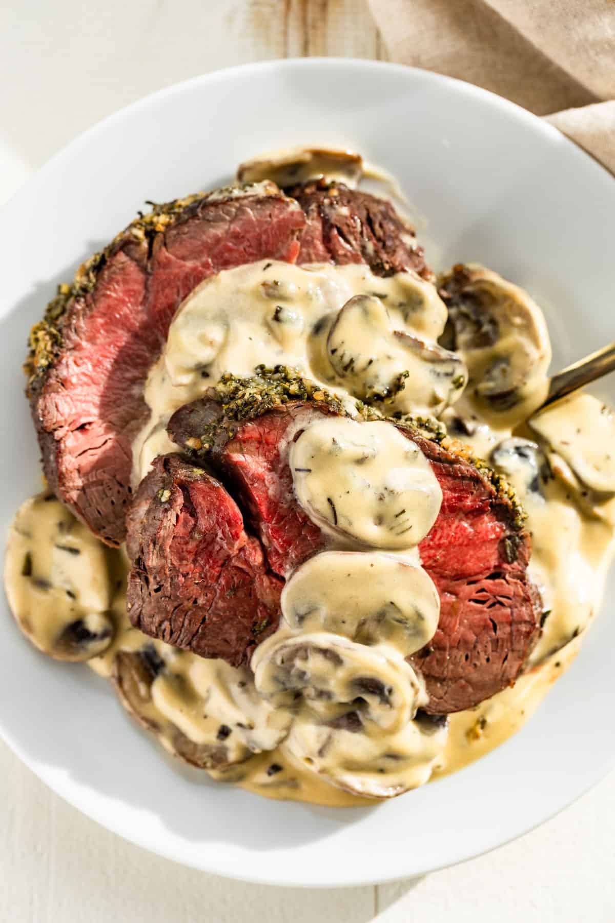 Sliced Beef Tenderloin roast on a white plate topped with mushroom cream sauce.