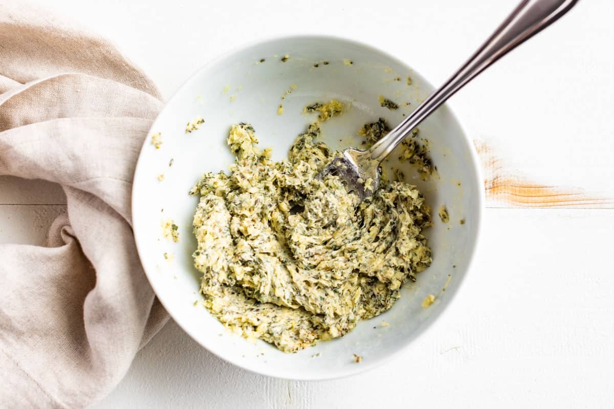 Garlic herb butter being mashed together in a medium white bowl.