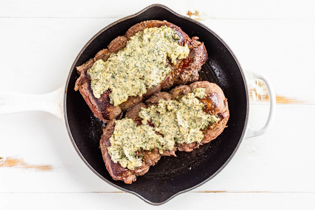 Spreading the garlic herb butter over the top of the browned Beef Tenderloin roasts in a cast iron skillet.