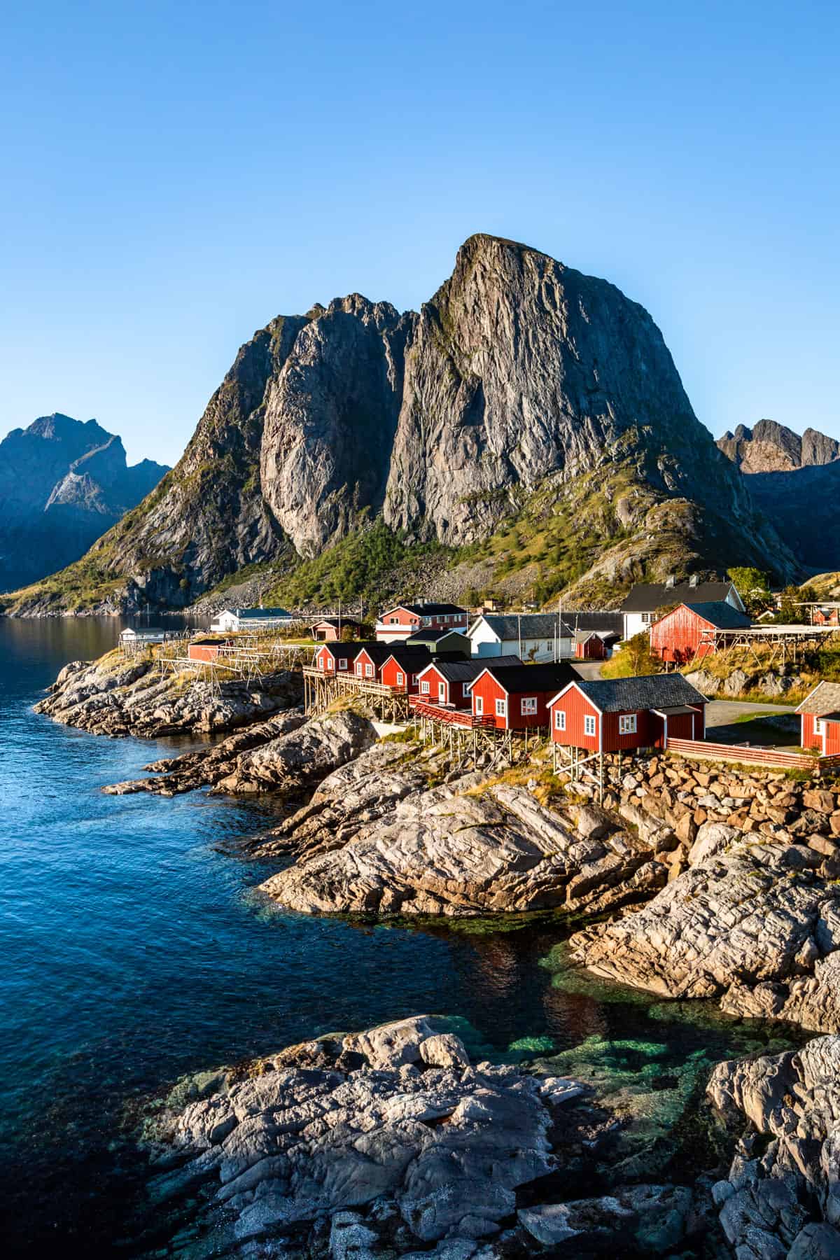 Photo of the famous red fisherman houses by the sea backed by mountains in the town of Reine, Norway.