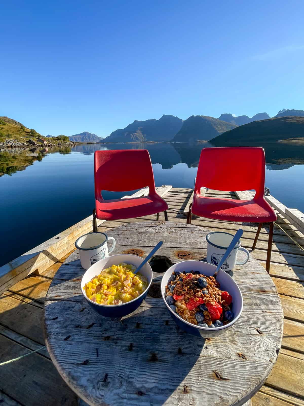 Two red plastic chairs around a table with a bowl of scrambled eggs and granola with berries sitting on a dock.