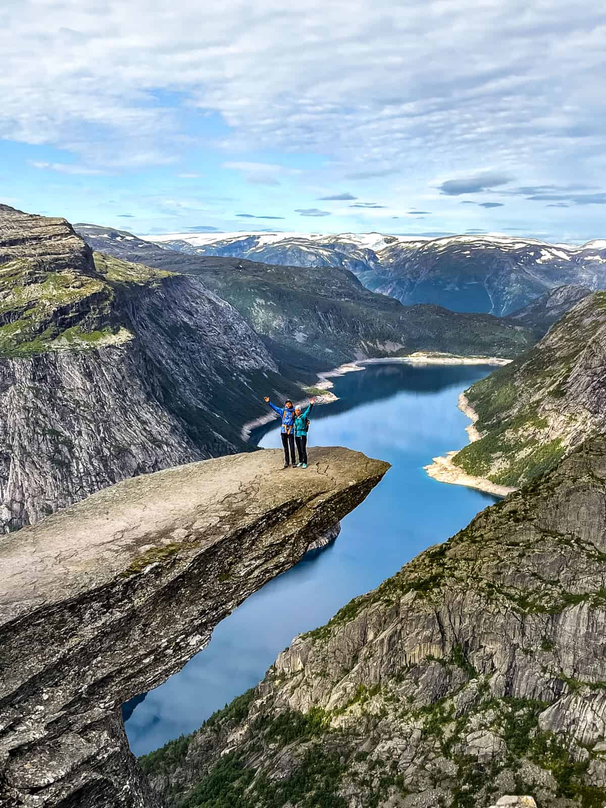 A couple standing on a large jutting rock over a fjord called Trolltunga.