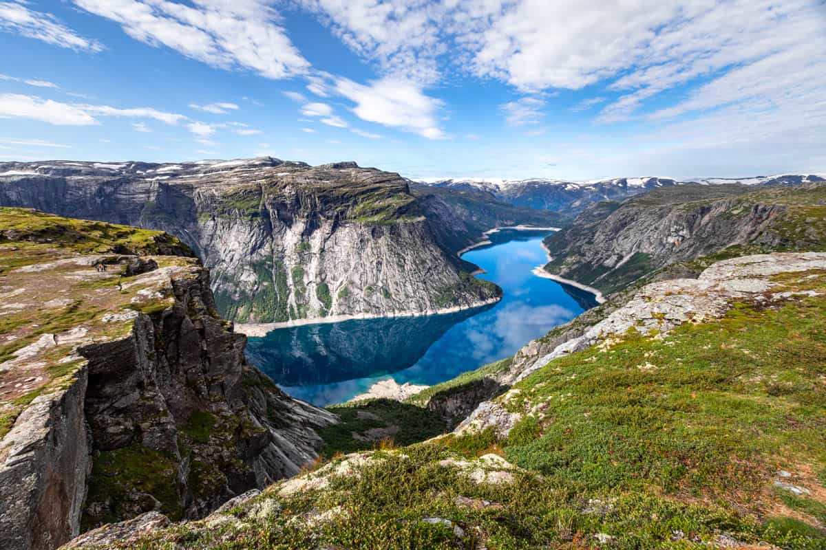 View of a deep blue fjord winding it's way through the mountains into the distance with light clouds on a sunny day.