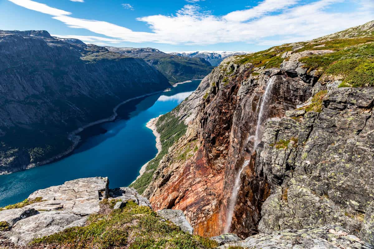 A view looking down a fjord in Norway with a waterfall pouring out of the side of the mountain.