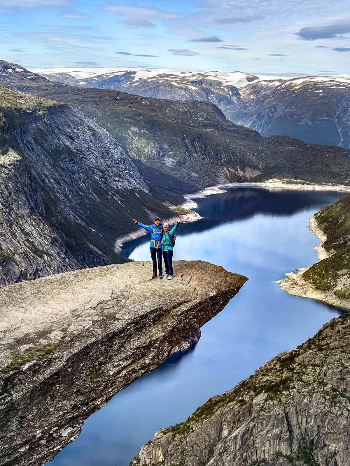 A couple standing on the Trolltunga hike in Norway overlooking a fjord.