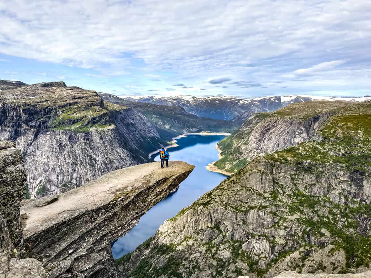 A couple standing on a rock outcropping over the fjord below.