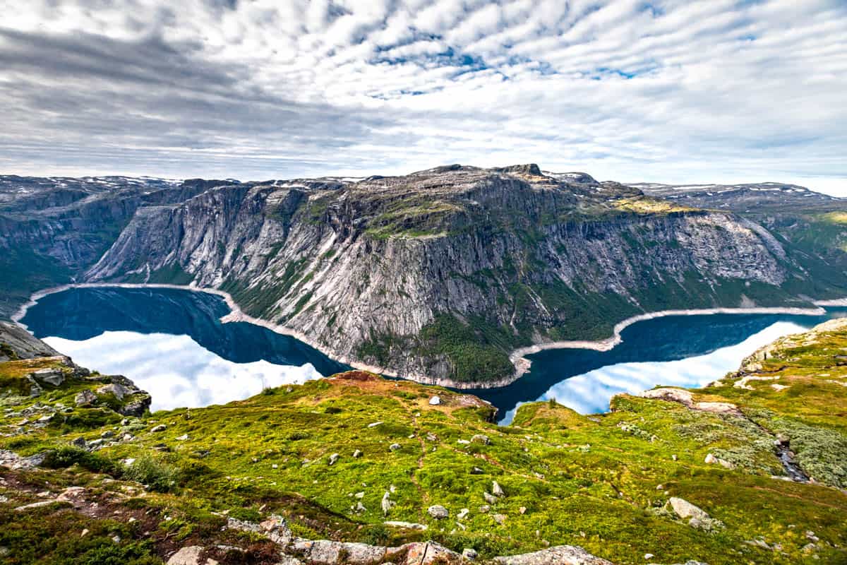 A long fjord stretching from the left to the right side of the photo with steep mountains in the background and sub alpine greenery in the foreground.