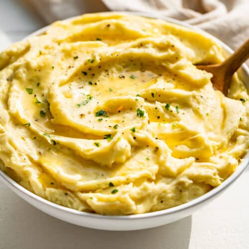 Side view of mashed potatoes in a white bowl topped with melted butter and chopped parsley.